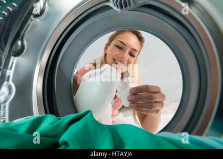 Young Smiling Woman Pouring Detergent In A Lid From Inside The Washing Machine Stock Photo