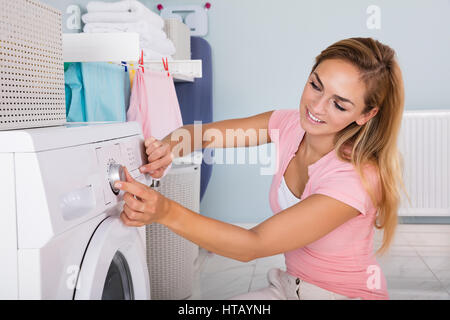 Young Smiling Woman Using Washing Machine To Clean Clothes In Laundry Room Stock Photo