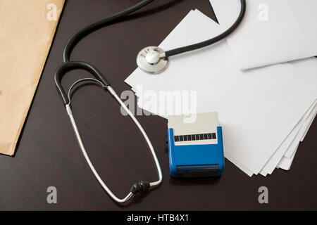Desk doctor. Stethoscope, stamp and documents laying on a dark table.  Doctor's office. Stethoscope, stamp, pen and medical history. Attributes of the Stock Photo