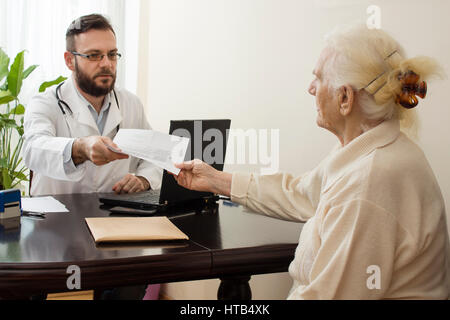 geriatrician doctor with a patient in his office. The doctor geriatrician with a patient. Receives documents from the patient. Stock Photo
