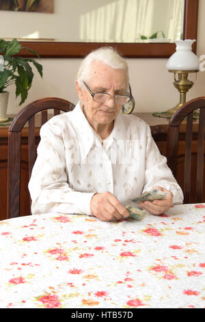 senior woman sitting at table with money, looking at camera and having ...