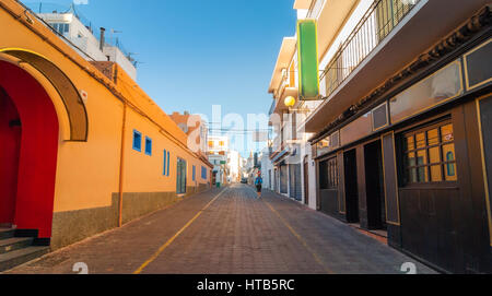 Glowing Warm tones from indirect afternoon sun.  Man walks down the road in the streets of St Antoni de Portmany, Ibiza, Balearic Islands, Spain. Stock Photo