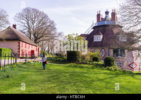 A single female walks towards a unique 16 sided 18th century building and thatched barn in early spring. Stock Photo