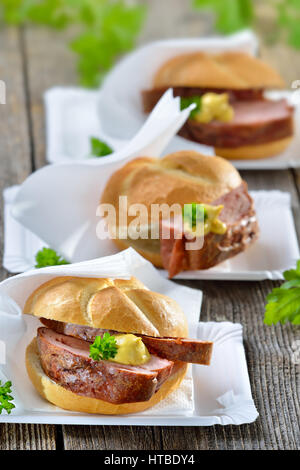 Bavarian takeaway food: Three rolls with baked meat loaf and mustard on paper plates
