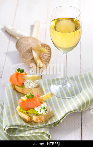 Delicious canapes with white asparagus, cream cheese with herbs, smoked salmon on Italian ciabatta bread with lettuce, served with a glass of wine Stock Photo