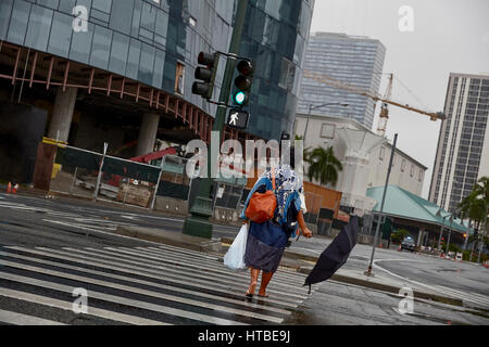 Honolulu; Hawaii; USA - August 7; 2016: An unidentified woman with umbrella crossing street in the rain under stormy skies in Honolulu, Oahu, Hawaii. Stock Photo