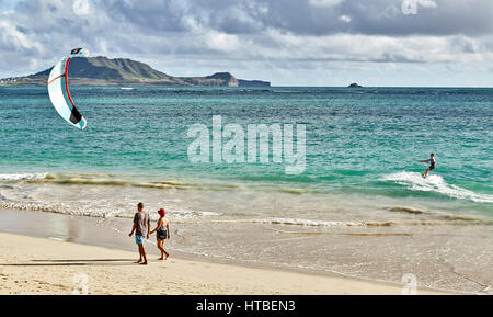 Kailua, Hawaii, USA - July 30, 2016: A man kitesurfs in the early morning while people walk by on the beach at Kailua Bay in Hawaii Stock Photo