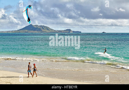 Kailua, Hawaii, USA - July 30, 2016: A man kitesurfs in the early morning while people walk by on the beach at Kailua Bay in Hawaii Stock Photo