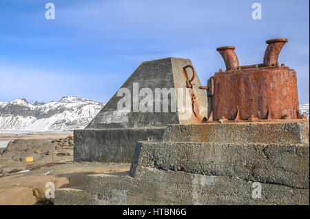 Close up of mooring cleat post on coastline at Dyrholaey, Iceland, in winter with blue sky and snow covered mountains in distance Stock Photo