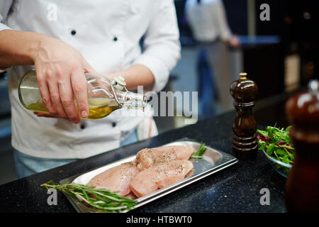 Chef pouring olive oil on raw chicken steak Stock Photo