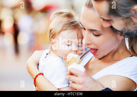 A baby boy is being hugged by his mother and father while fed with ice cream. Stock Photo