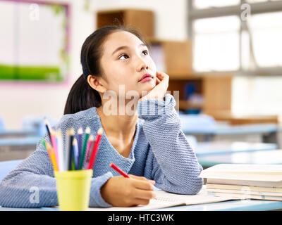 asian elementary schoolgirl looking up and thinking while studying in classroom. Stock Photo