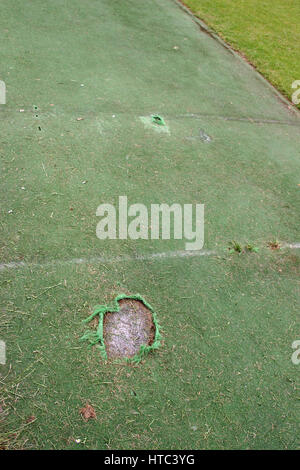 Damaged artificial cricket wicket with crease lines and holes for the stumps. Large tear in the bowling crease and smaller tear in the batting crease. Stock Photo