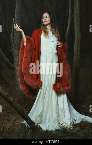 Beautiful young woman posing with elegant red cloak. Fantasy woods Stock Photo