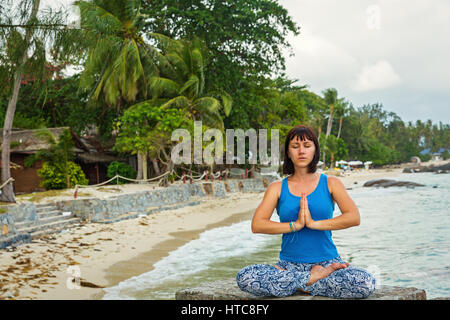 Young woman doing yoga sitting on a rock on the sea shore Stock Photo