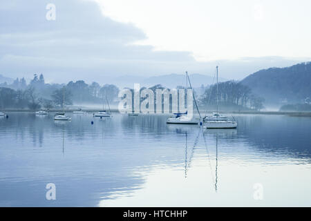 Boats in mist at sunset on a winter's day, with reflections, Lake Windermere at Waterhead, Ambleside, Lake District, Cumbria, UK Stock Photo