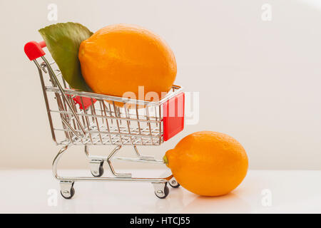 Mini cart, trolley shopping witch organic fresh vegetables, two ripe lemons on light background. Concept of healthy food shopping, detox, dieting, veg Stock Photo