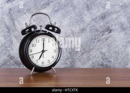 7 o'clock vintage clock on wood table and concrete wall background Stock Photo