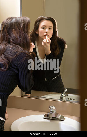 Woman putting on lipstick in restroom Stock Photo