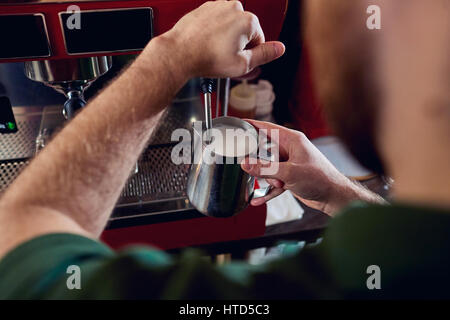 Bartender, barista makes hot milk in a coffee machine behind the bar closeup. Stock Photo