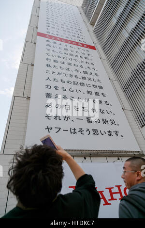 A man takes pictures of a huge banner on display outside Sony building in Ginza on March 11, 2017, Tokyo, Japan. The banner displayed by Yahoo Japan Corp. is marked with a red line at 16.7 meters, the actual height of tsunami which hit the northeast coast of Japan on March 11, 2011. 2017 marks the sixth anniversary of the earthquake and tsunami that killed thousands and led to the Fukushima nuclear crisis. Credit: Rodrigo Reyes Marin/AFLO/Alamy Live News Stock Photo