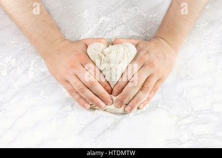 A man's hands kneading dough in the form of a heart, with flour on a marble table, with a place for text Stock Photo