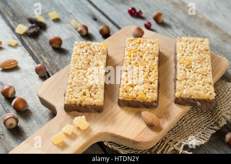 Muesli bars with dry fruits and chocolate layer on a wooden cutting board, closeup view Stock Photo