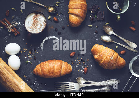 Coffee, croissants, chocolate, spices, nuts and vintage cutlery. Flat lay composition of sweet breakfast food on dark stone background with copy space Stock Photo