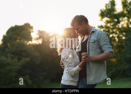 Affectionate young couple dancing hand in hand together while enjoying a romantic moment on sunny summer afternoon in a park Stock Photo