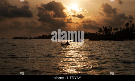Silhouette of one man rowing a small boat with his paddle on the ocean at sunset, Belitung Indonesia. Stock Photo
