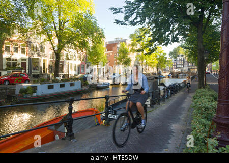 Cycling to work along one of Amsterdam's canal tow paths, on a sunny morning Stock Photo