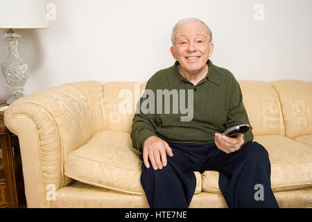 Elderly man on sofa with remote control Stock Photo