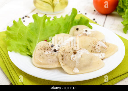 Italian ravioli (dumplings) in the shape of a heart on a plate on white wooden background. Stock Photo