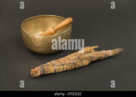 Bronze Tibetan Singing Bowl with Wooden Ringing Stick and Large Native American Smudge Stick on a Black Background. Stock Photo