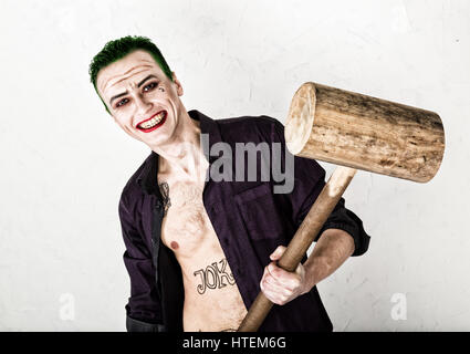 guy with crazy joker face, green hair and idiotic smile. carnaval costume. holding hammer for cricket. Stock Photo