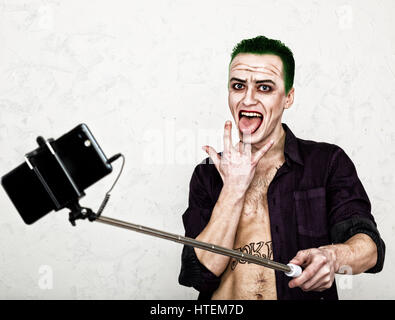 guy with crazy joker face, green hair and idiotic smile. carnaval costume. making selfy photo. Stock Photo