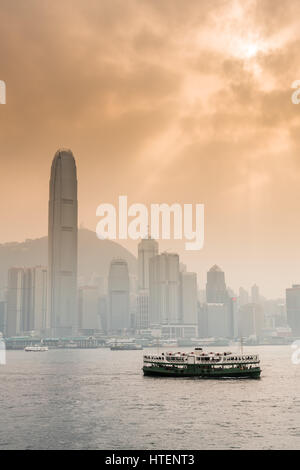 Ferry in the Victoria Harbour with the skyscrapers and the Hong Kong skyline, with the sun shining through dramatic clouds. China. Stock Photo