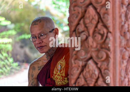 Phnom Kulen, Cambodia - January 03, 2017: Portrait of a tattooed Buddhist monk in traditional robe behind a column of Phnom Kulen pagoda Stock Photo