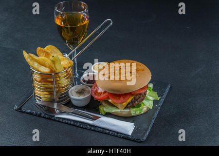 right side view on a flame grilled double stack cheeseburger, lettuce, tomato, with three sauces, chips in a metal basket, white wine, tasty set Stock Photo