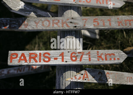 Wooden signpost on ground showing which way is Paris and New York. It is very old and left on the ground even it has some broken pices but it looks am Stock Photo