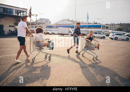 Young friends having fun on a shopping carts. Multiethnic young people playing with shopping cart. Stock Photo