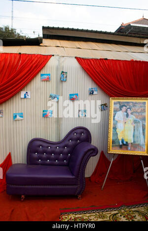 Small wedding photographs are attached to a wall behind a purple sofa in a wedding reception area in Chork Village, Cambodia. Stock Photo