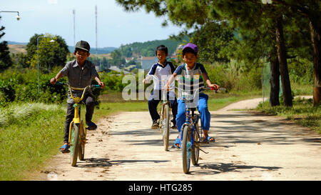 LAM DONG, VIET NAM-  DEC 28, 2016: Group of unidentified Vietnamese children ride bicycle on country road at noon, naughty boy run to tease his friend Stock Photo