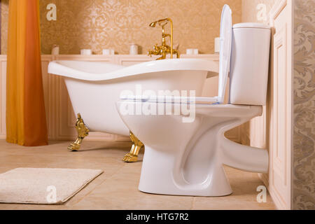 Luxury sanitary equipment with gold elements. Rich bath with gold roll-tops in the form of animal paws, golden faucet and toilet in the bathroom. Stock Photo