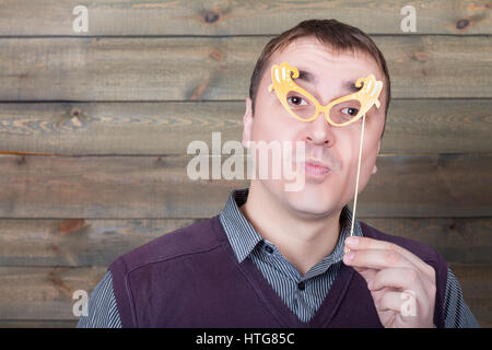 Young man with funny glasses on a stick, wooden background. Fun photo props and accessories for shoots Stock Photo