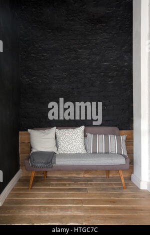 Grey sofa with large pillows with different print standing black brick wall Stock Photo