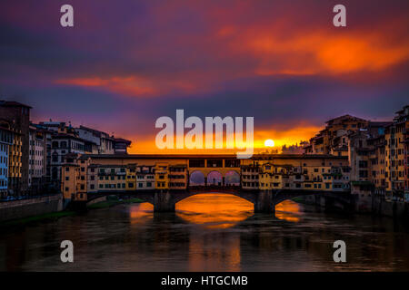 Clearing storm clouds at dawn create a dramatic sunrise over the Ponte Vecchio bridge in Florence, Italy with the sun peeking between clouds. Stock Photo