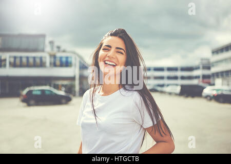 Laughing woman in white blouse and long hair standing in the middle of large parking lot outdoors Stock Photo