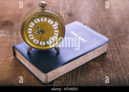 Holy Bible and old gold alarm clock on wood table. Vintage colore. Stock Photo