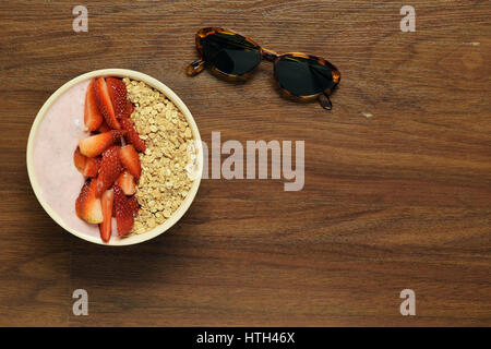 Top view of muesli bowl strawberries and yoghurt. Sun glasses. Healthy breakfast. Summer concept. Stock Photo